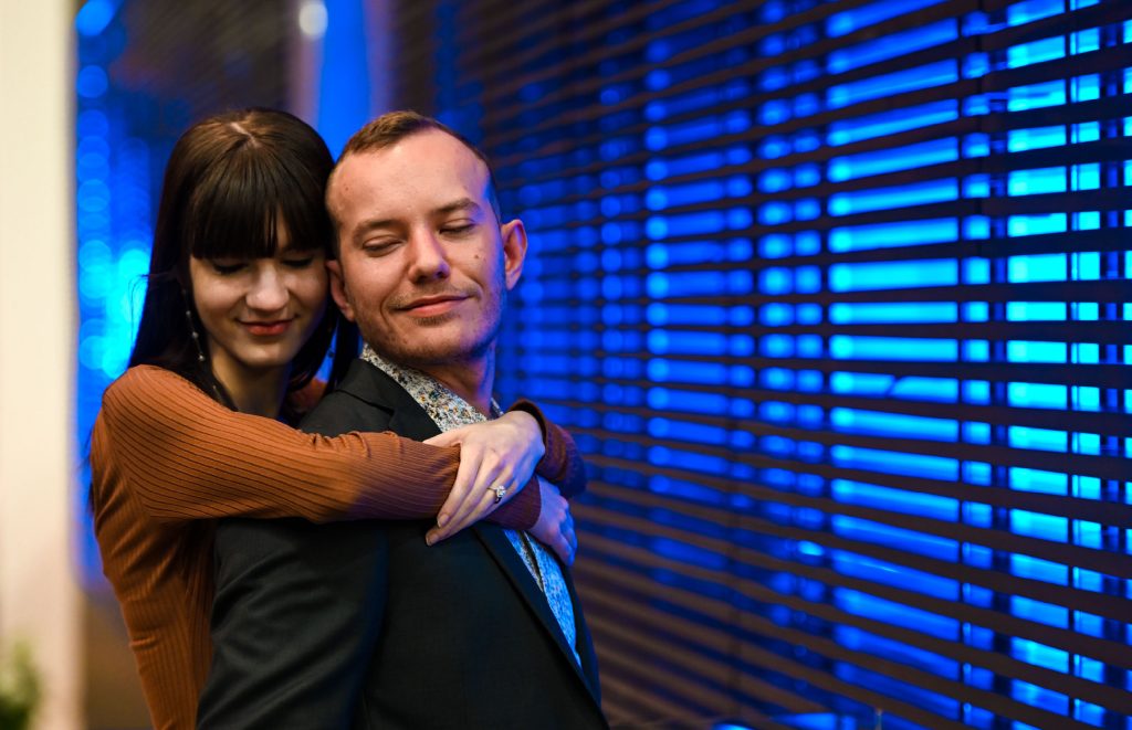 A woman wearing an engagement ring embraces her fiancé.
