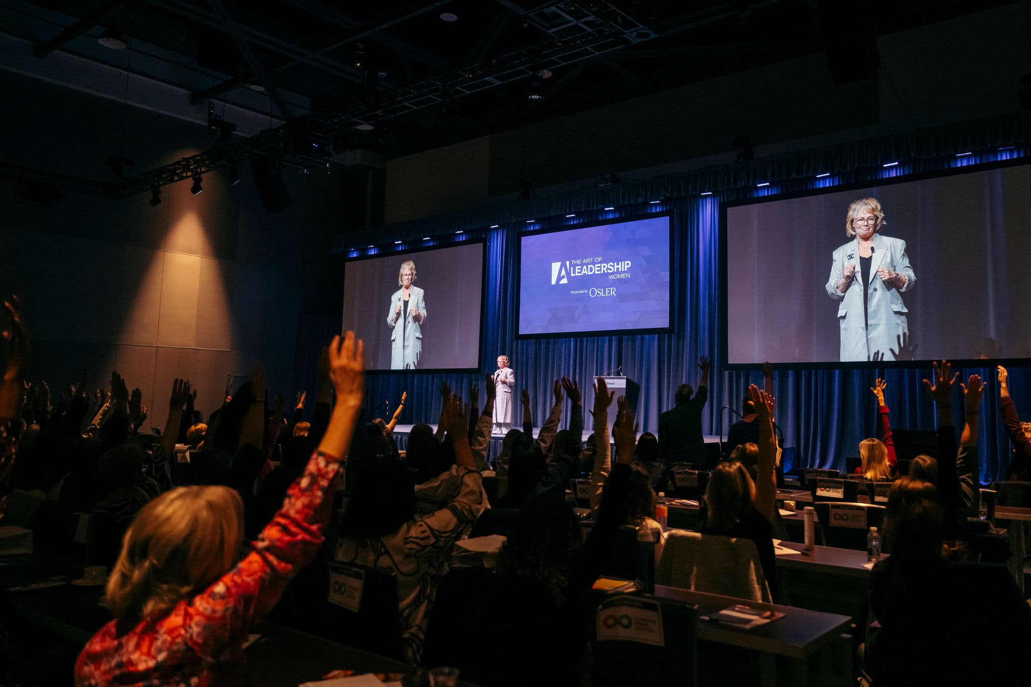 Arlene Dickinson, stands on stage, attendees raise their hand to show consensus with what Arlene said
